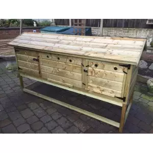 6ft British Giant XL Rabbit Hutch + Stand, featuring multiple compartments and a slanted roof secured with metal latches, similar to a predator-safe wooden chicken coop placed on a paved surface.