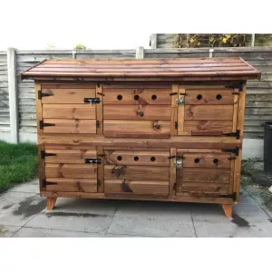 The 6ft British Giant XL Double Rabbit Hutch, featuring wire doors and complete winter protection, is situated on a concrete patio surrounded by a wooden fence and grassy area. It offers multiple compartments and metal latches, making it perfect for keeping your furry friends cozy during the winter months.