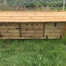 The 6ft British Giant XL Rabbit Hutch, crafted from wood and designed for outdoor use, is placed on green grass. It features a sloped roof, locking door, and two additional compartments.