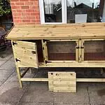 Wooden multi-level rabbit hutch with hinged doors, wire mesh panels, and a removable side panel on a patio, designed to ensure optimal winter rabbit care.