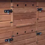 This wooden structure, ideal for winter rabbit care, boasts multiple sections with several black metal latches and circular ventilation holes.