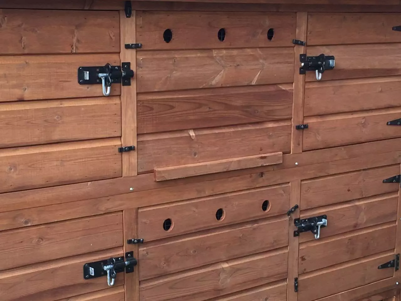 This wooden structure, ideal for winter rabbit care, boasts multiple sections with several black metal latches and circular ventilation holes.